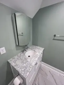 A closeup look at the wash basin with mirror on top with white cabinets below.